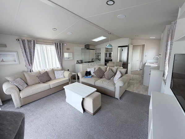 A modern living room with two sofas, a coffee table, and a kitchen in the background. - Ambleside Lodge Sleeps 6 With Parking and Wrap Around Balcony (Porthmadog)