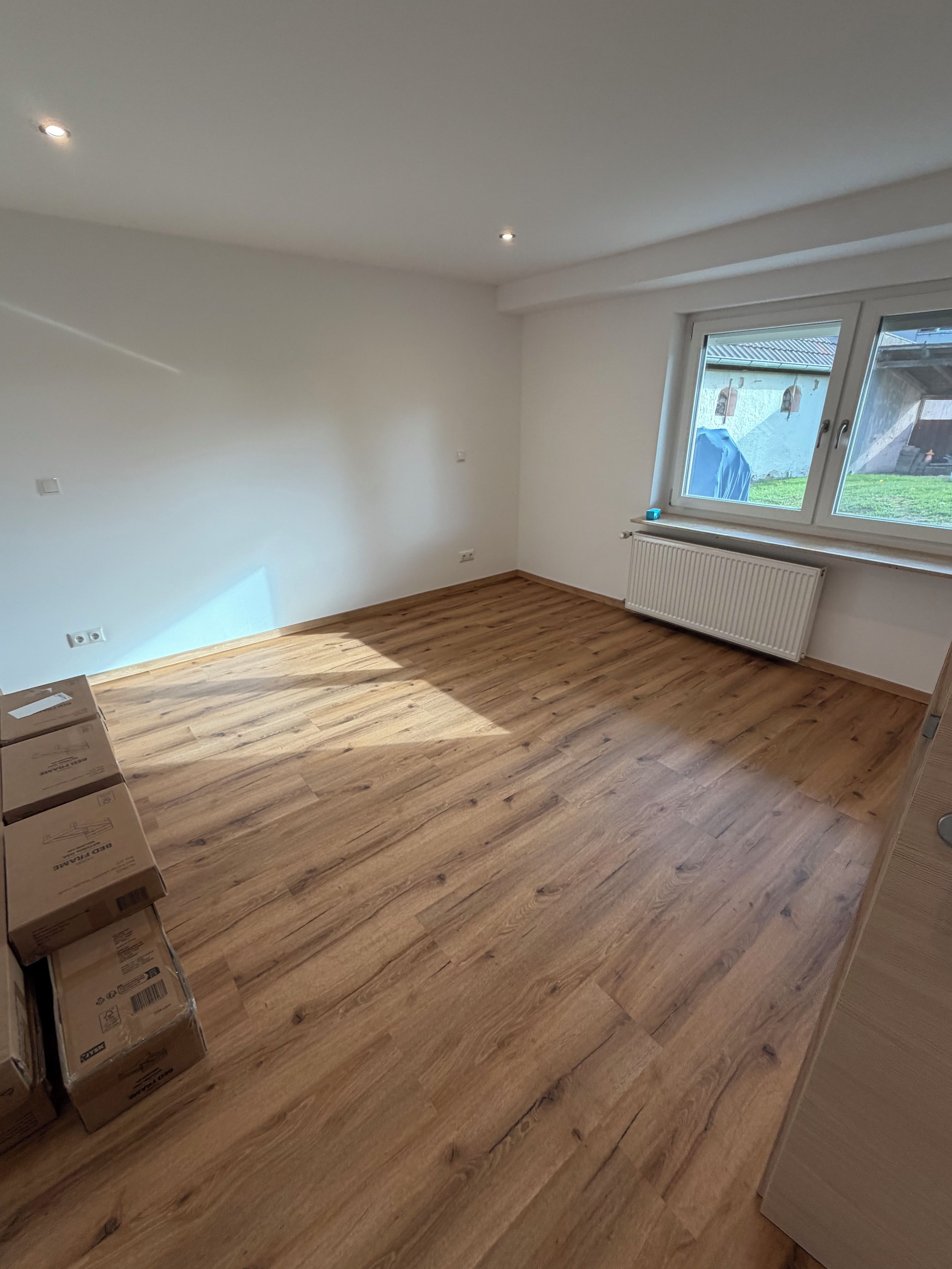 Une pièce avec un plancher en bois, une fenêtre donnant sur un paysage agréable et plusieurs cartons.