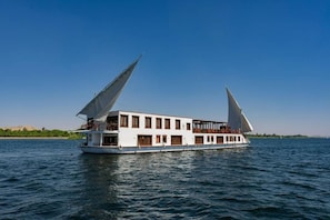 Et hvidt flodskib med flere dæk og store sejl, der flyder på stille vand.