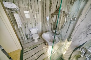 Et badeværelse med marmorgulv, toilet i hvidt, vask og brusekabine i glas.
