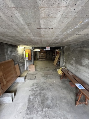 Un interior de formigó amb una banca de fusta, un senyal de precaució groc i una porta de fusta.