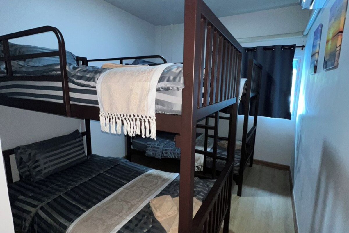 A bunk bed room with a ceiling light, a window with curtains, and an air conditioning unit on the wall.