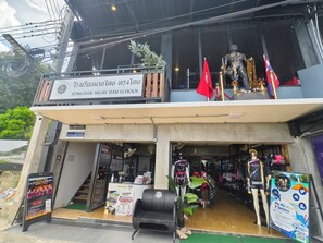 Un edificio con un letrero que indica Songthai Muay Thai School, que cuenta con la entrada a una tienda, maniquíes y banderas.