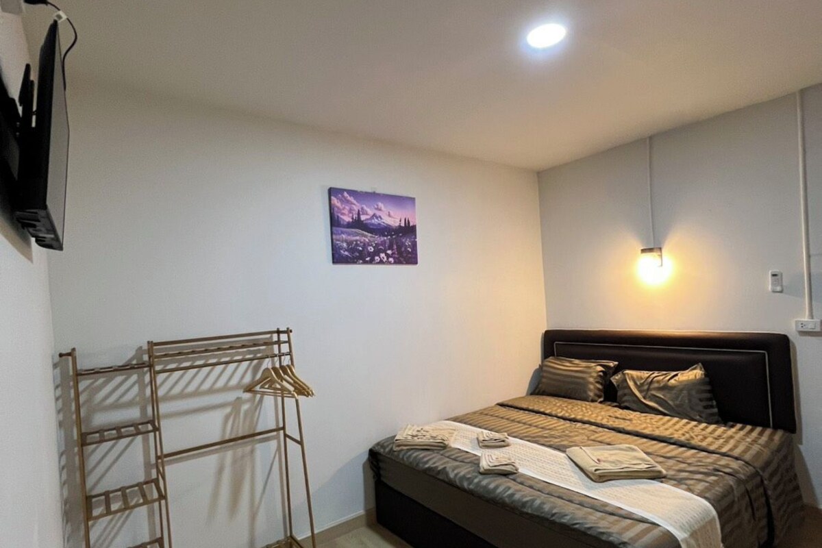 A bedroom with a bed, a wall-mounted TV, a picture, and a light fixture.