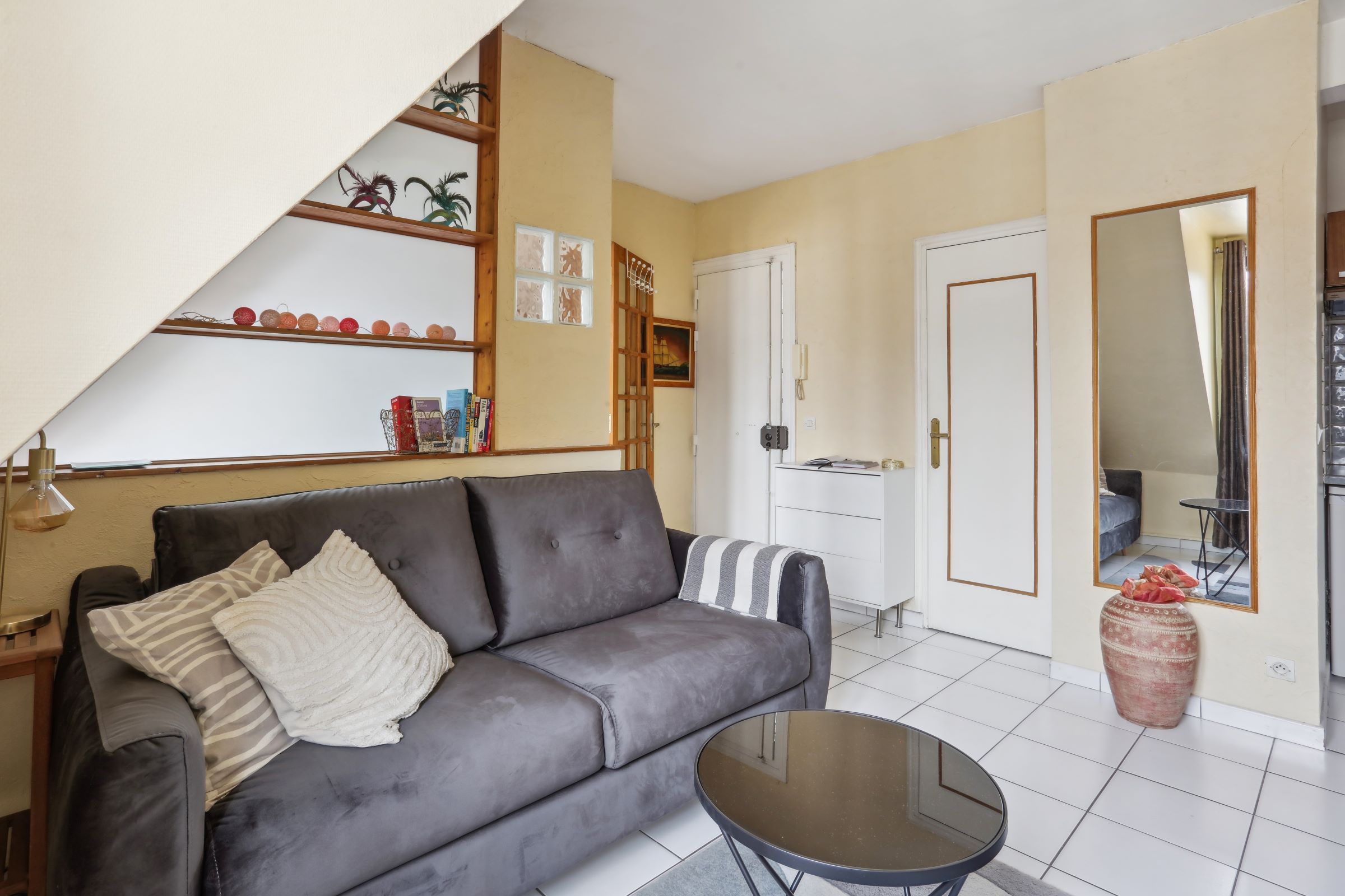 Ein Wohnzimmer mit grauem Sofa, einem kleinen Couchtisch und einem Bücherregal mit Dekoration.