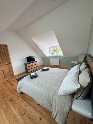 Une chambre avec un plafond en pente, un lit avec des oreillers, une commode, un téléviseur et une fenêtre.