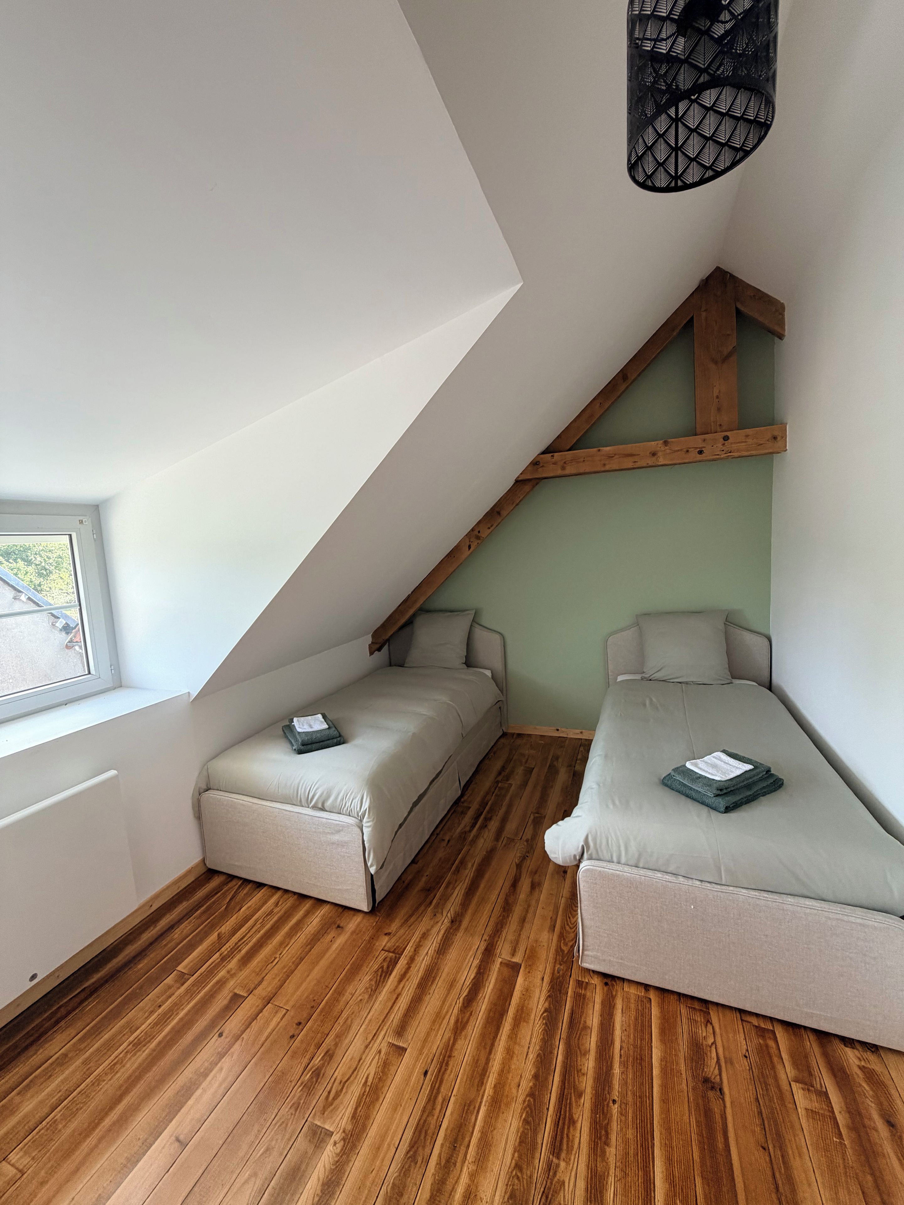 A small, cozy room with two beds, a sloped ceiling, and a window.