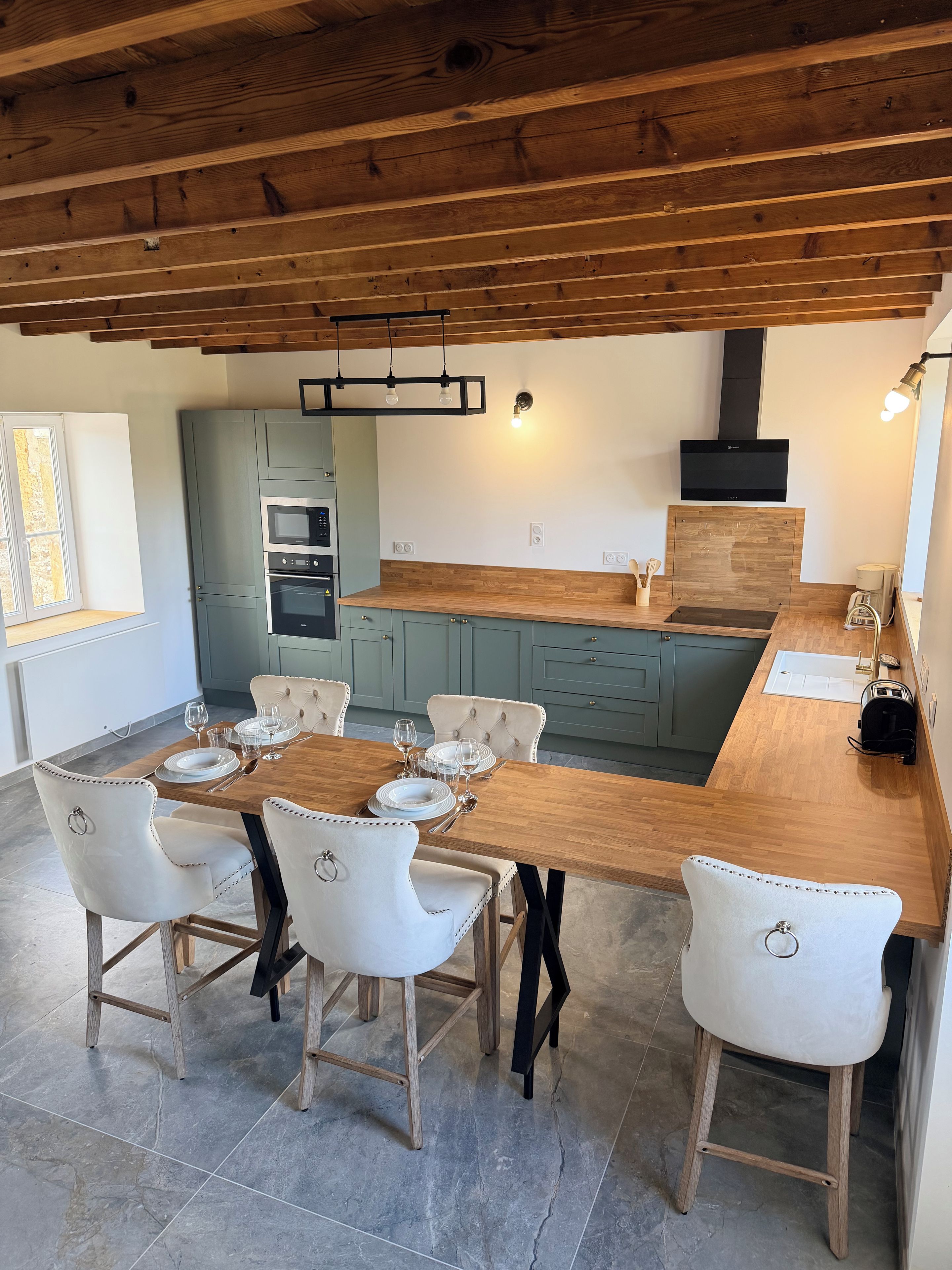 A modern kitchen with a wooden ceiling, built-in appliances, and a dining area with white chairs and a wooden table.