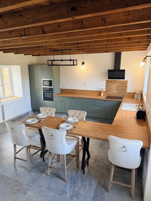 Une cuisine moderne avec un plafond en bois, des appareils électroménagers intégrés et un coin repas avec des chaises blanches et une table en bois.