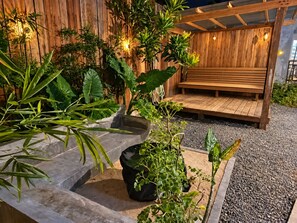 Een houten bank onder een pergola, met potplanten en een muur met verticale houten latten.