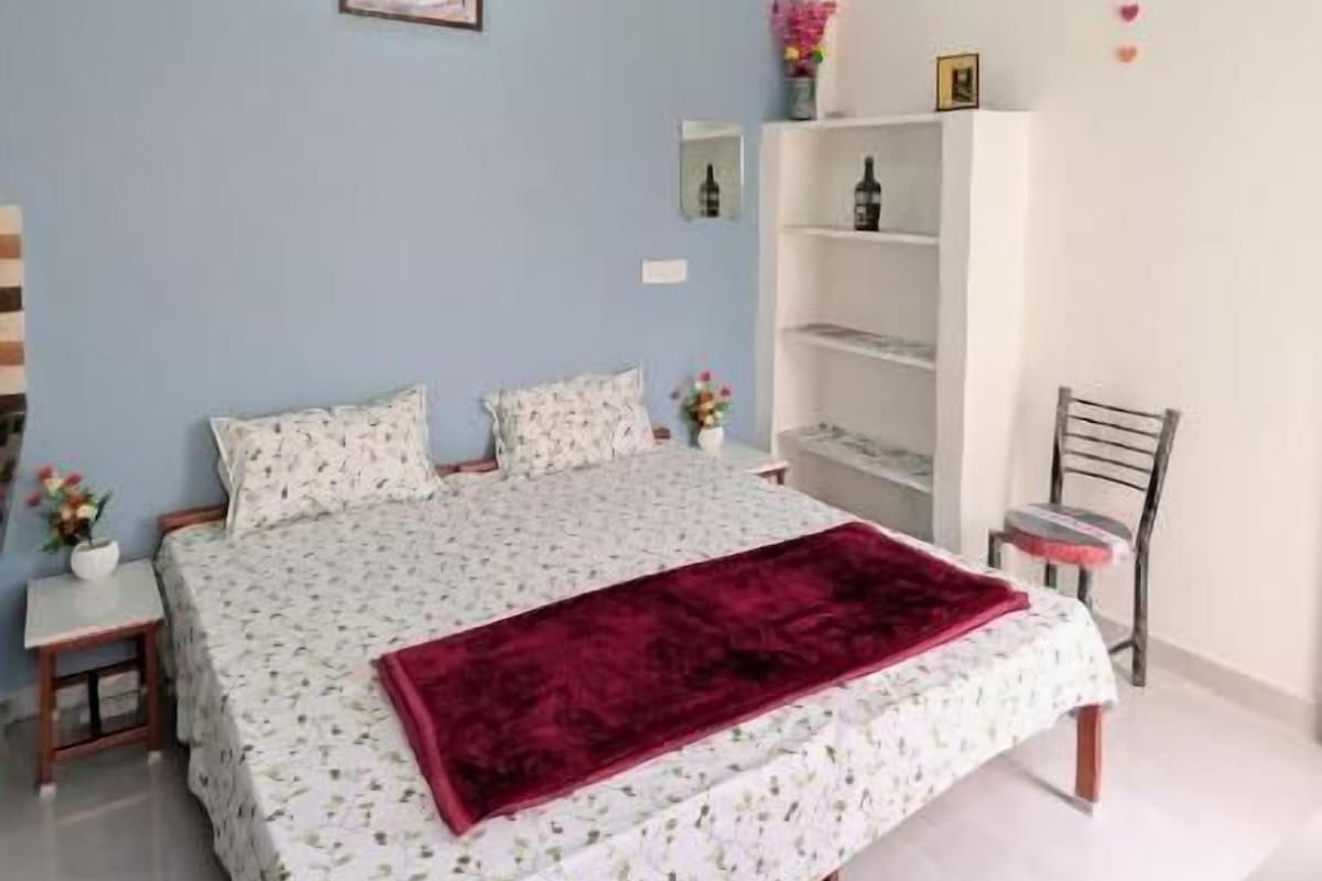 Une chambre à coucher comprenant un lit, un ventilateur de plafond, une table de chevet, une chaise et une bibliothèque.