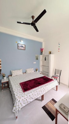 Une chambre à coucher comprenant un lit, un ventilateur de plafond, une table de chevet, une chaise et une bibliothèque.