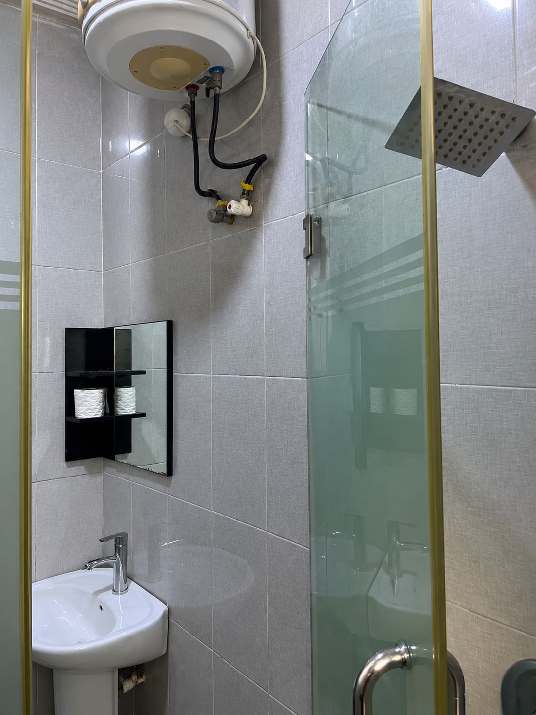 A bathroom with a glass shower enclosure, a white sink, and a mirror with a black frame.