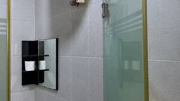 A bathroom with a glass shower enclosure, a white sink, and a mirror with a black frame.