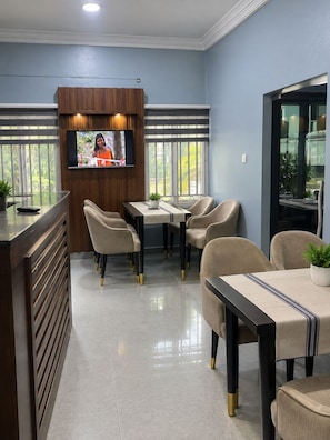 A modern hotel lobby with a reception desk, seating area, and a television mounted on a wooden panel. - Alpines Hotels and Reservations (Port Harcourt)