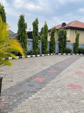 A paved courtyard with a patterned tile floor, surrounded by a low wall with vertical greenery and a palm tree. - Alpines Hotels and Reservations (Port Harcourt)