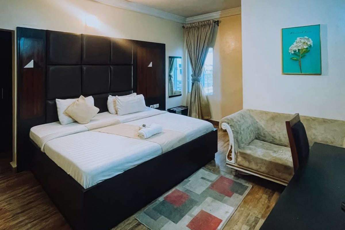 A hotel room with a bed, a sofa, a small table, and a painting on the wall.