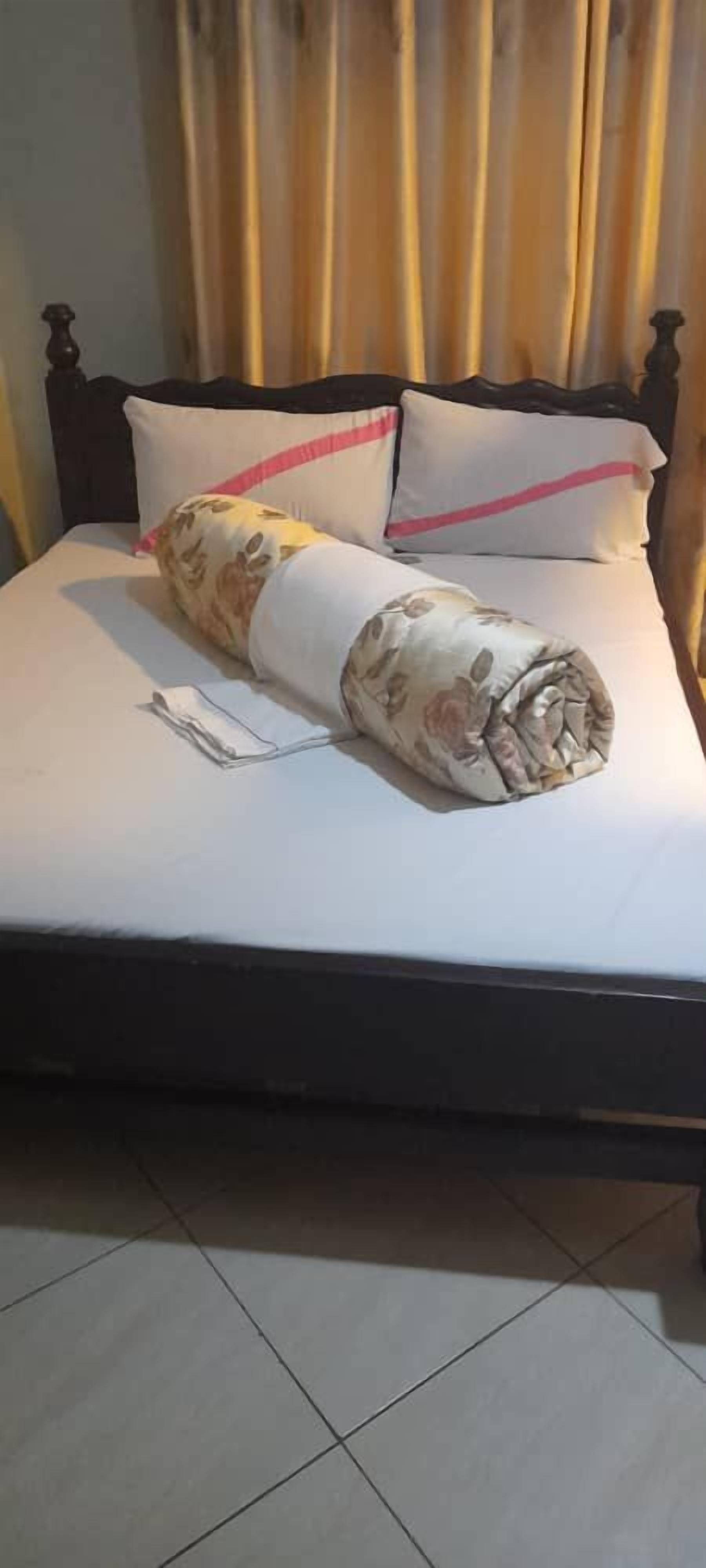 A bed with a rolled blanket and a pillow, a bedside table, and a curtain.