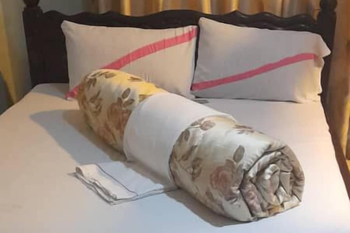 Un letto con una coperta arrotolata, un cuscino, un comodino e una tenda.