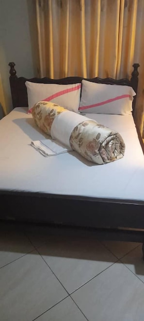 Un letto con una coperta arrotolata, un cuscino, un comodino e una tenda.