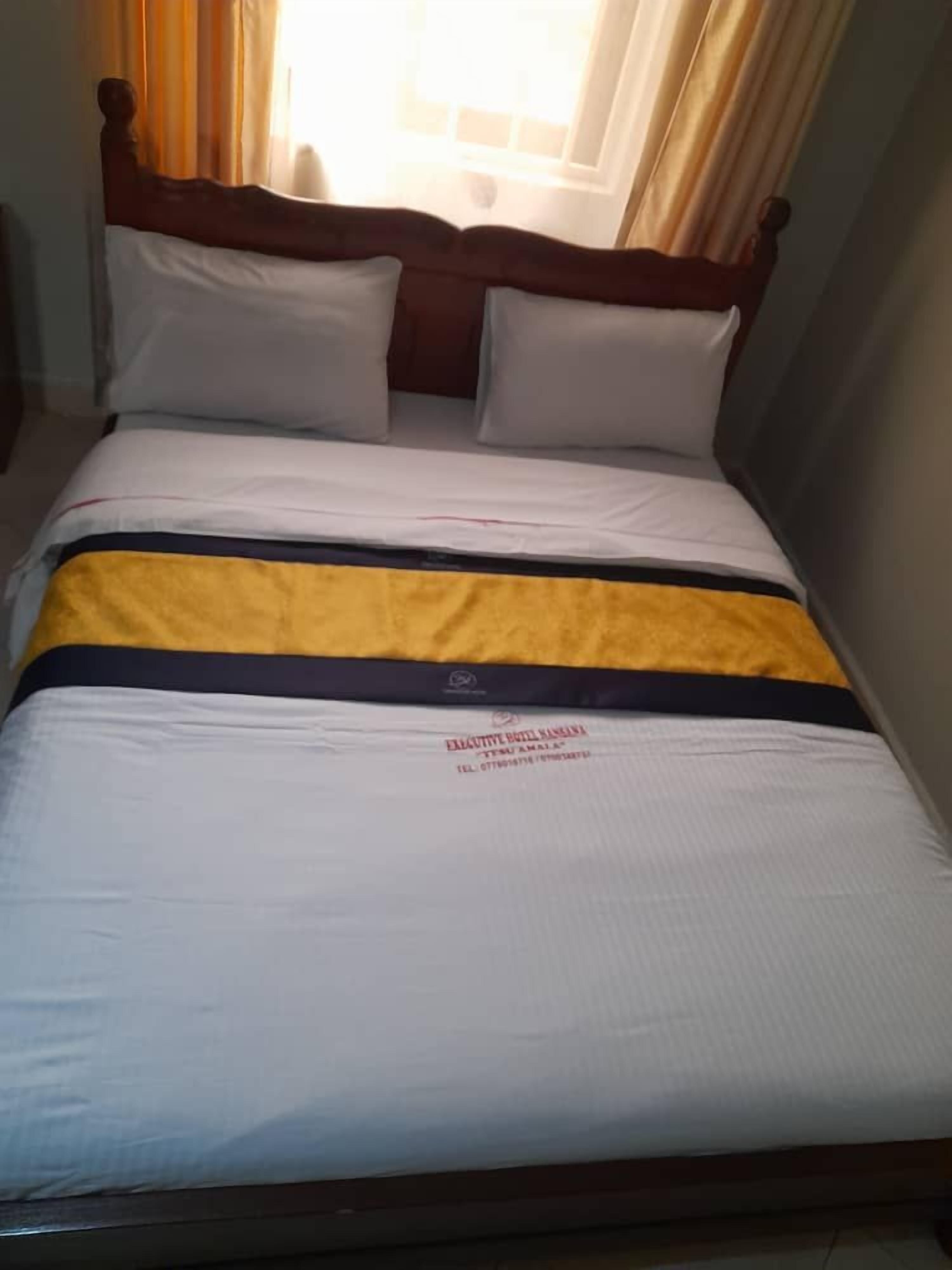 A bed with a wooden headboard, white bedding, and a yellow and black striped blanket.