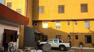 Un hotel con fachada amarilla y un letrero que dice 'BK HOTEL'. Un camión pickup blanco está estacionado al frente, y hay mesas dispuestas para comer con manteles y sillas blancos.