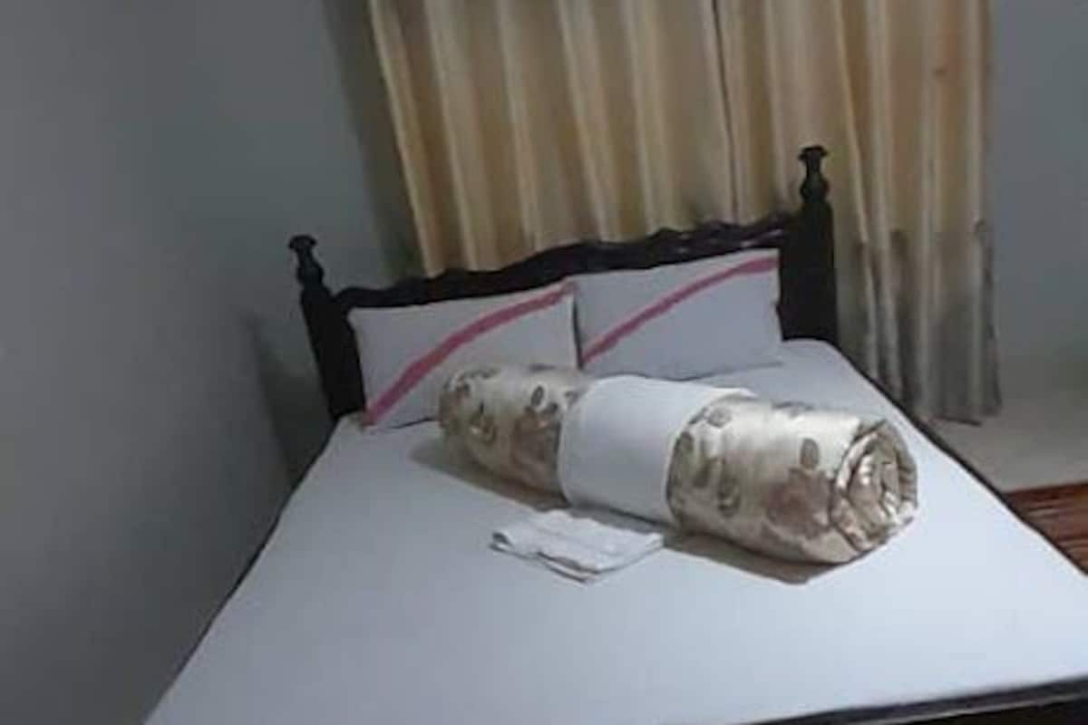 Un letto con materasso bianco, una coperta arrotolata, un cuscino e un comodino con una lampada.