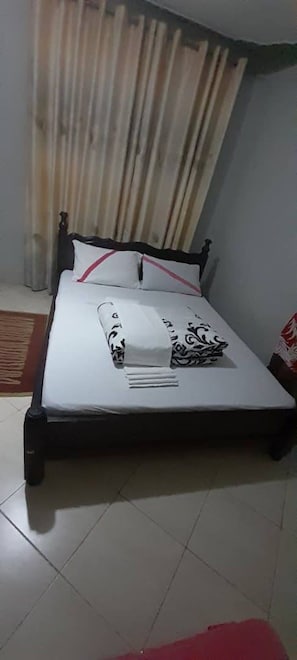Un letto singolo con struttura nera, biancheria bianca e un cuscino rosso.