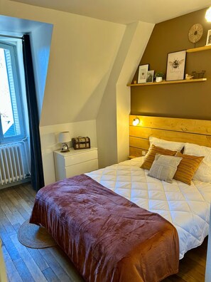 A bedroom with a bed, a nightstand, a chest of drawers, a window, and a wall-mounted shelf with decorative items. - New Listing (La Bourboule)