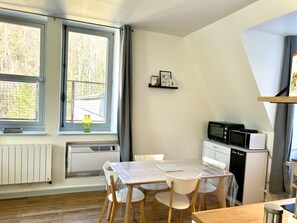 A compact kitchen with a dining table, chairs, a microwave, and a small refrigerator. - New Listing (La Bourboule)