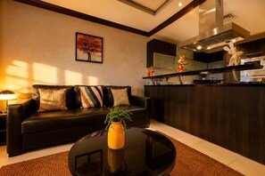 Una sala de estar moderna con un sofá de cuero negro, una mesa redonda de centro con un jarrón amarillo y una zona de cocina con extractor de acero inoxidable.