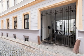 A building entrance with a metal gate, a bicycle parked inside, and a cobblestone street. - Wagner 12 Old Town Apartment - 2 bedrooms, sleeps 5, Wi-Fi (Rīga)