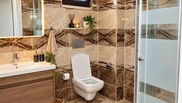 A modern bathroom with a marble backsplash, a toilet, a sink with a mirror, and a shower area.