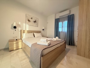 Habitació d'hotel amb llit, taules de nit, aire condicionat fixat a la paret i una finestra amb cortines.