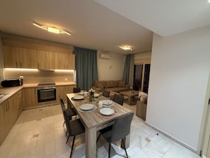Una cuina moderna amb armaris de fusta, una taula de dinar preparada per a quatre i una zona de estar amb un sofà i taula de centre.
