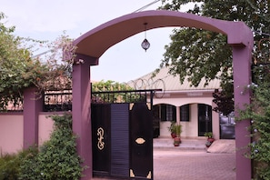Un cancello con arco decorativo, una telecamera di sicurezza e un edificio con tetto in tegole e piante in vaso.