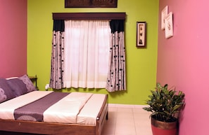 Een slaapkamer met een bed, gordijnen, een potplant en een wand met een fotolijst.