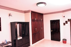 Een kamer met een grote kledingkast, een deur en een klein tafeltje met een strijkijzer.