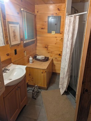 Une salle de bain rustique, aménagée dans une cabane en bois, avec un lavabo, un panier à serviettes, un radiateur et un rideau de douche.