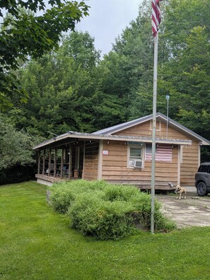 Une petite cabane en bois avec un porche, un drapeau américain et un chien dans la cour.