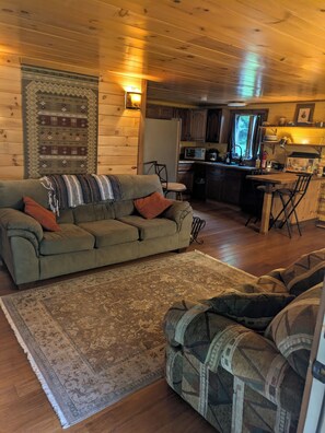 L’intérieur d’un chalet accueillant, avec un canapé, un tapis et un coin cuisine.