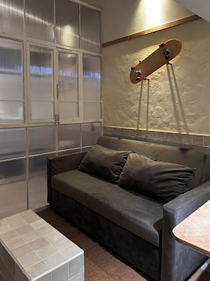 Una habitación con un sofá gris, un banco blanco y un monopatín sujeto a la pared.