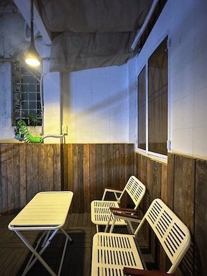 Un espacio de estar techado al aire libre con una mesa, sillas, una lámpara colgante y un ventanal.