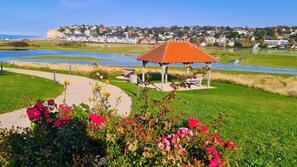 A gazebo in a park with a pathway and flowers in the foreground. - New Listing (Petit-Caux)