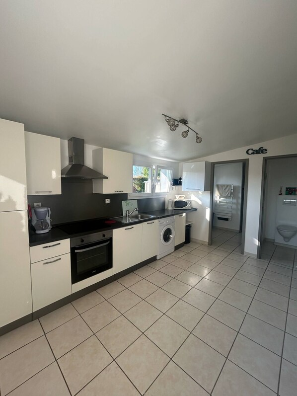 A modern kitchen with white cabinets, a black countertop, a built-in oven, a microwave, and a washing machine. - New Listing (Petit-Caux)