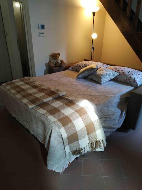 A bedroom with a bed, a lamp, a teddy bear, and a checkered blanket. - New Listing (Comacchio)