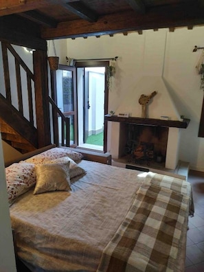 A bedroom with a bed, a wooden staircase, a fireplace, and a view through a door. - New Listing (Comacchio)