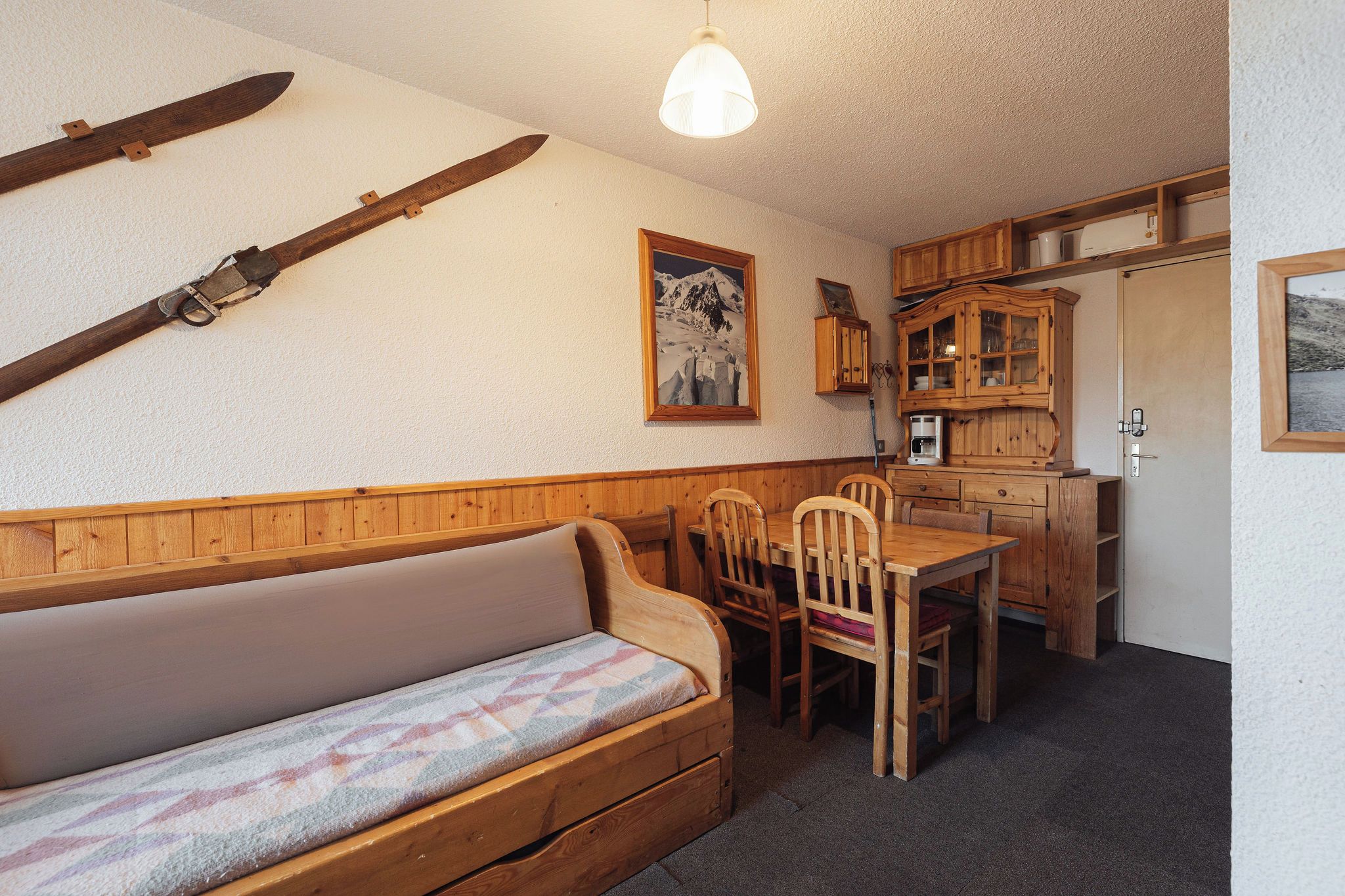 Ein gemütliches Zimmer mit einer Holzbank, einem Esstisch mit Stühlen und einer Küchenzeile mit Holzschränken.