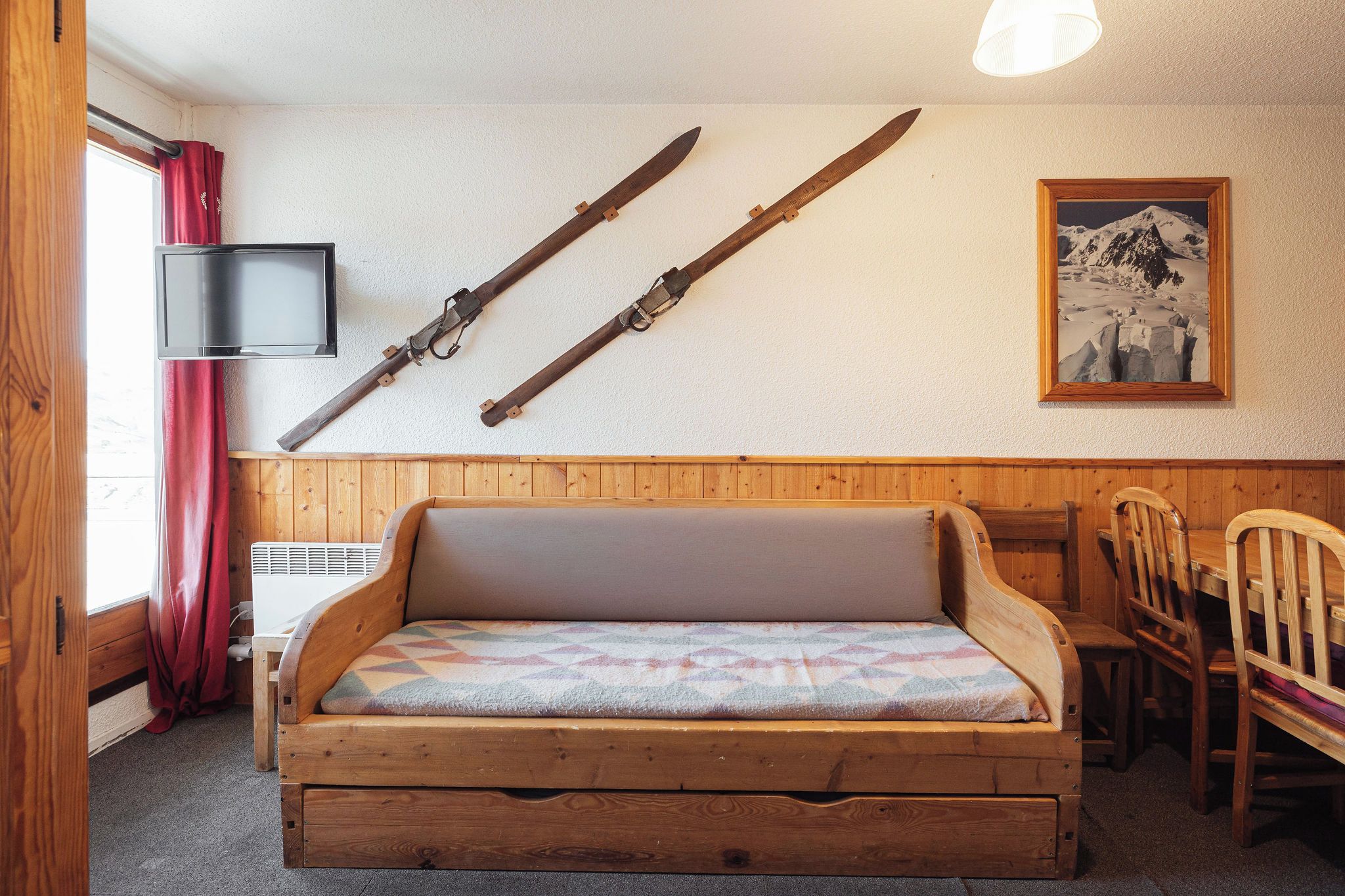 Una cama nido de madera con colchón, una silla de madera, un esquí sujeto a la pared y un cuadro enmarcado.