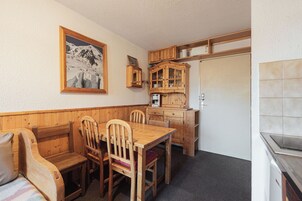 Una habitación acogedora con una mesa de comedor de madera, sillas, un banco y una zona de cocina con armarios y una cafetera.